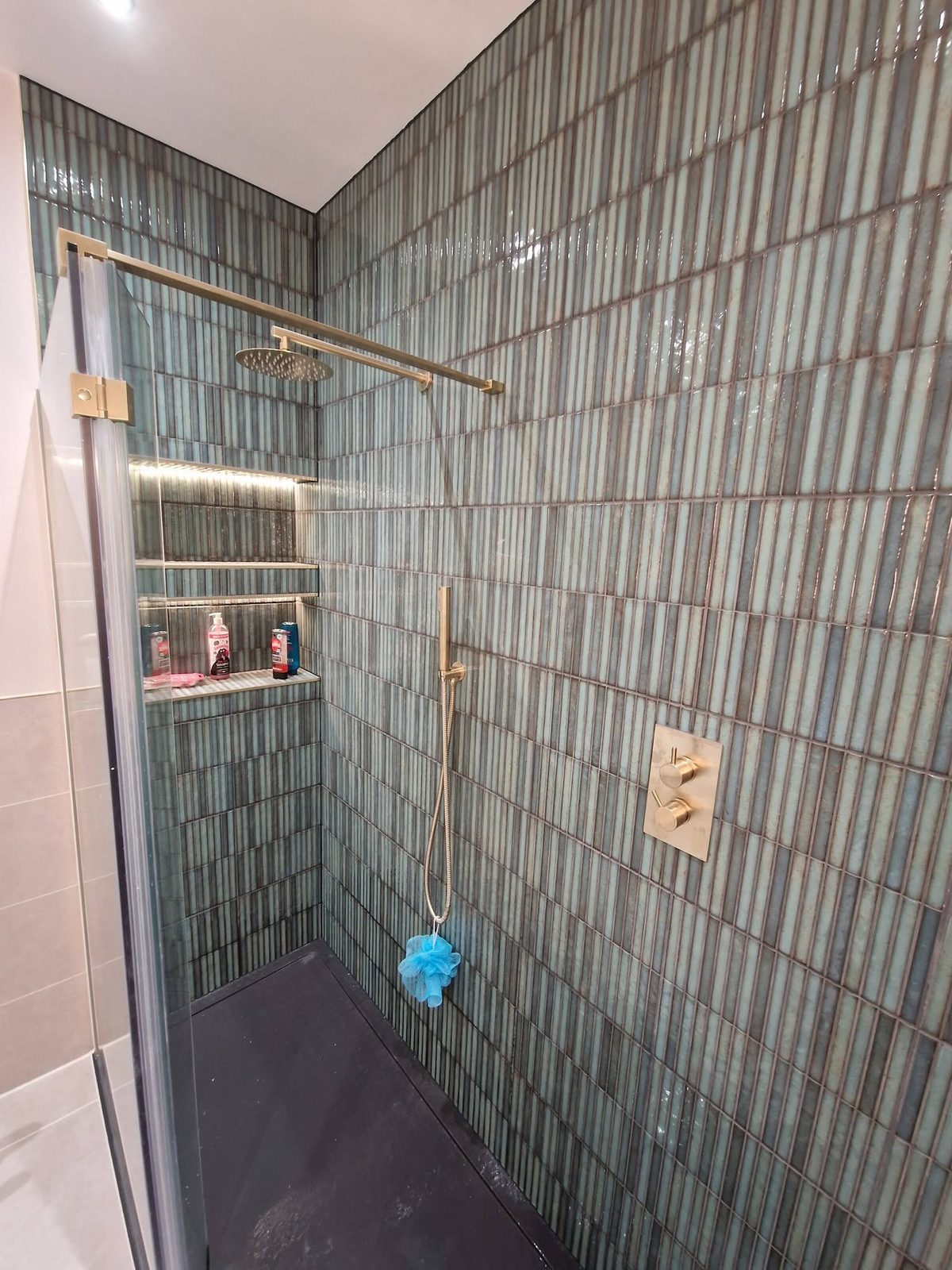 Walk-in shower with green stacked tiles and a lit niche
